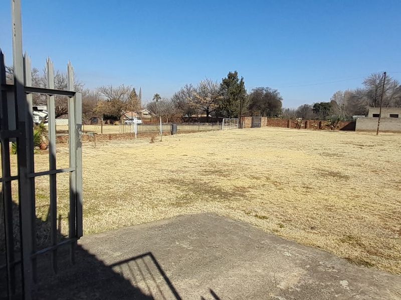 A spacious rear yard featuring a concrete patio area, enclosed by brick boundary walls and metal security fencing.