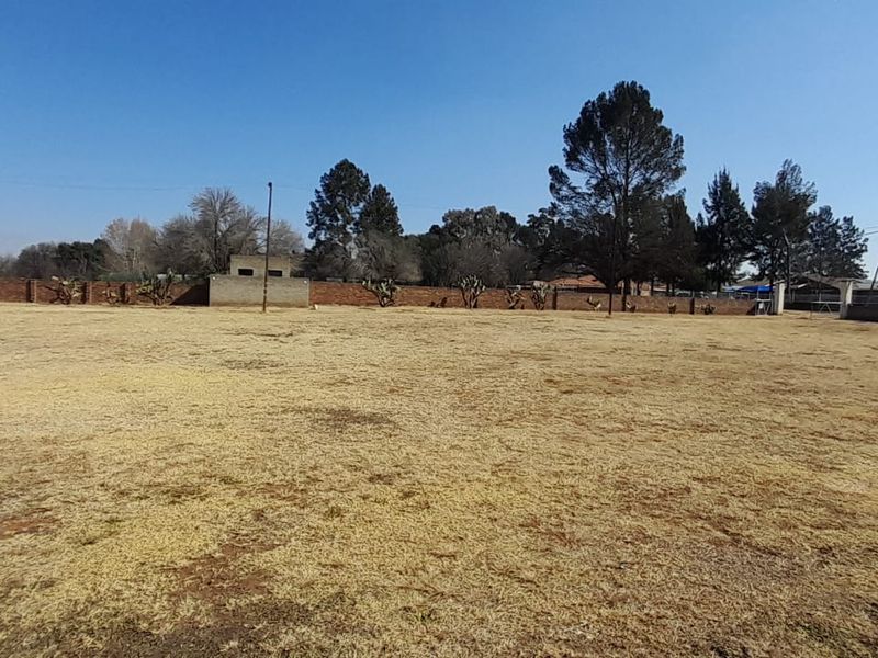 A large, open, and level garden area enclosed by a brick perimeter wall with mature trees in the background.