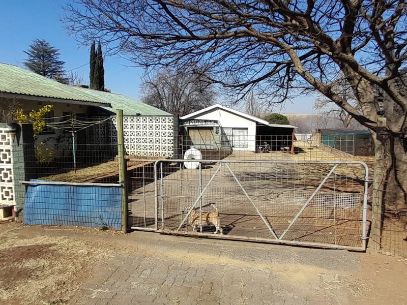 Front exterior view of the property featuring a metal gate, wire fencing, concrete driveway, and a house with a corrugated metal roof.