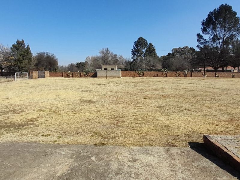 A spacious, open garden area featuring a large lawn, brick boundary walls, and perimeter fencing, providing a blank canvas for landscaping.
