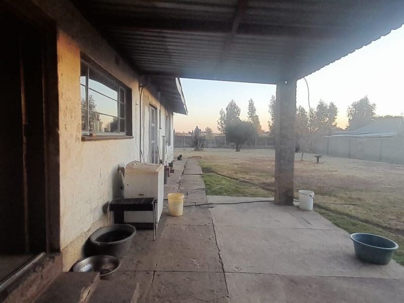 A covered outdoor patio area featuring a concrete floor and brick support pillar, showing signs of significant weathering and wear.