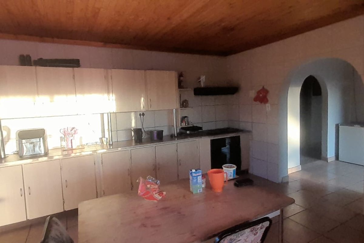 A dated kitchen featuring extensive built-in cabinetry, tiled backsplash, and a timber ceiling, leading through an archway to an adjacent space.