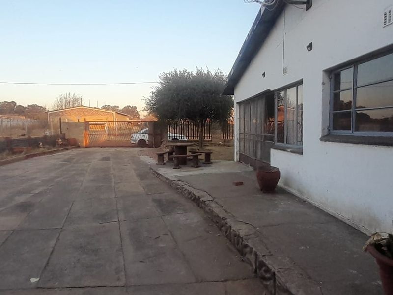 Rear exterior view of the property featuring a large paved driveway, concrete patio area, and perimeter security fencing.