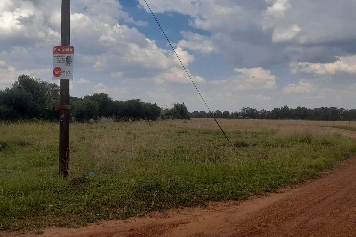A view of a vacant residential plot featuring a dirt road access and existing utility infrastructure.