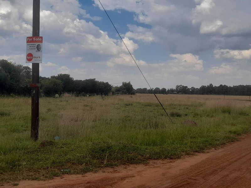 A view of a vacant residential plot featuring a dirt road access and existing utility infrastructure.