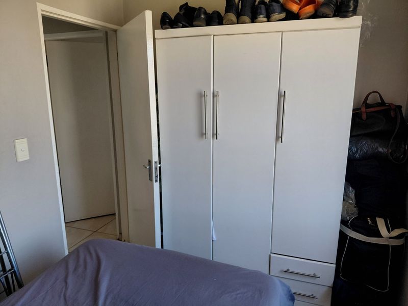 A bedroom featuring a white three-door built-in wardrobe with metal handles and lower drawers.