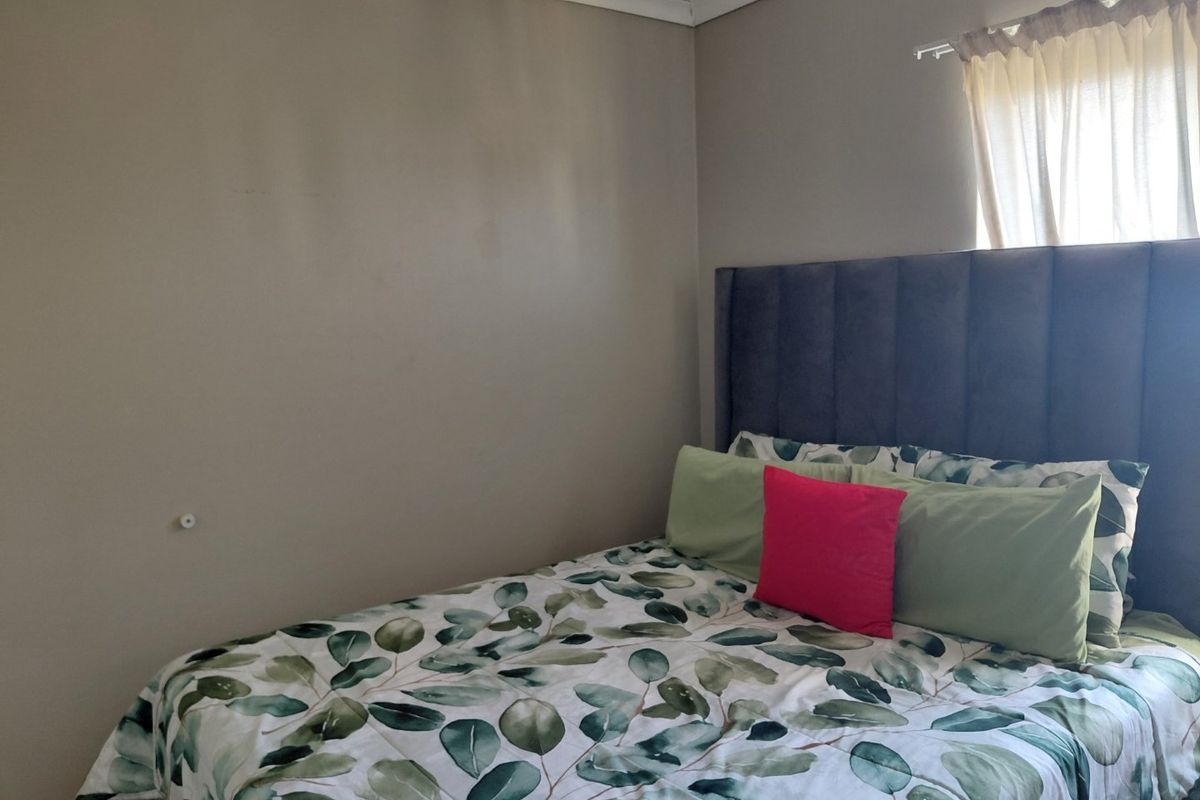 A simple bedroom featuring neutral wall tones, coving, and a window with a fitted curtain rod.