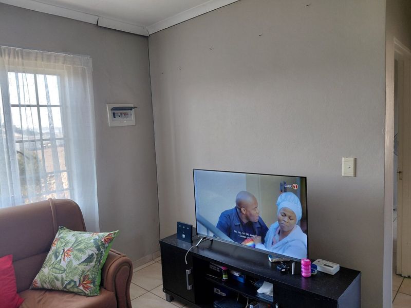 Living room area featuring tiled flooring and an exposed electrical distribution board, showing signs of wear on the ceiling cornice and walls.