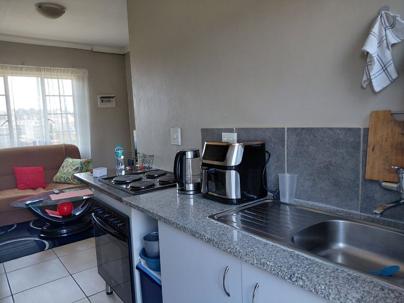 Open-plan kitchen and living area featuring granite countertops, a stainless steel sink, built-in oven, electric hob, and tiled flooring.