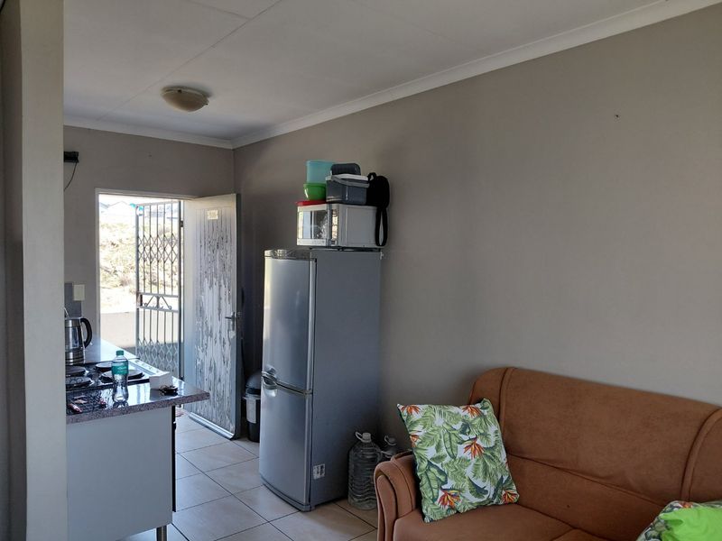 Open-plan living area featuring tiled floors, a compact kitchen counter with a hob, and direct access to an exterior security gate.