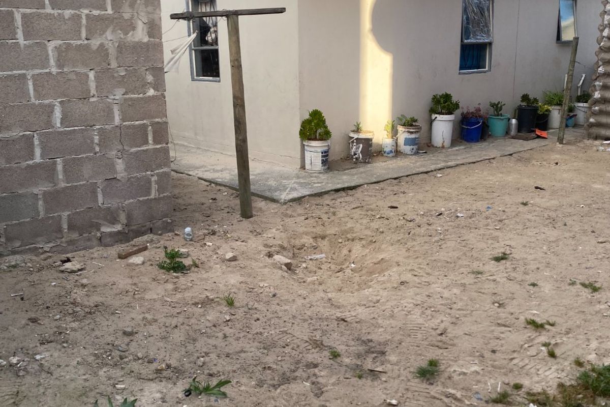Rear exterior view of the property featuring a concrete block boundary wall, tiled roof, and an unlandscaped sandy yard area.