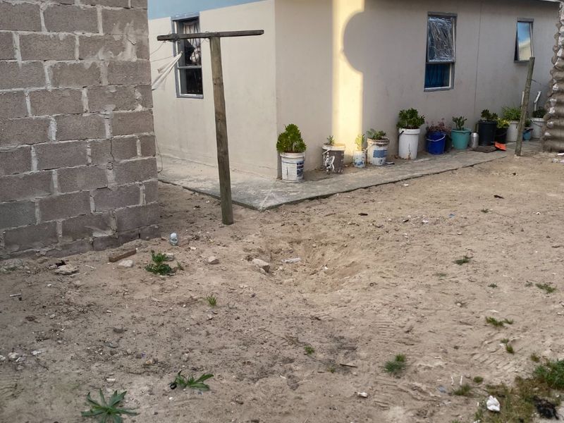 Rear exterior view of the property featuring a concrete block boundary wall, tiled roof, and an unlandscaped sandy yard area.