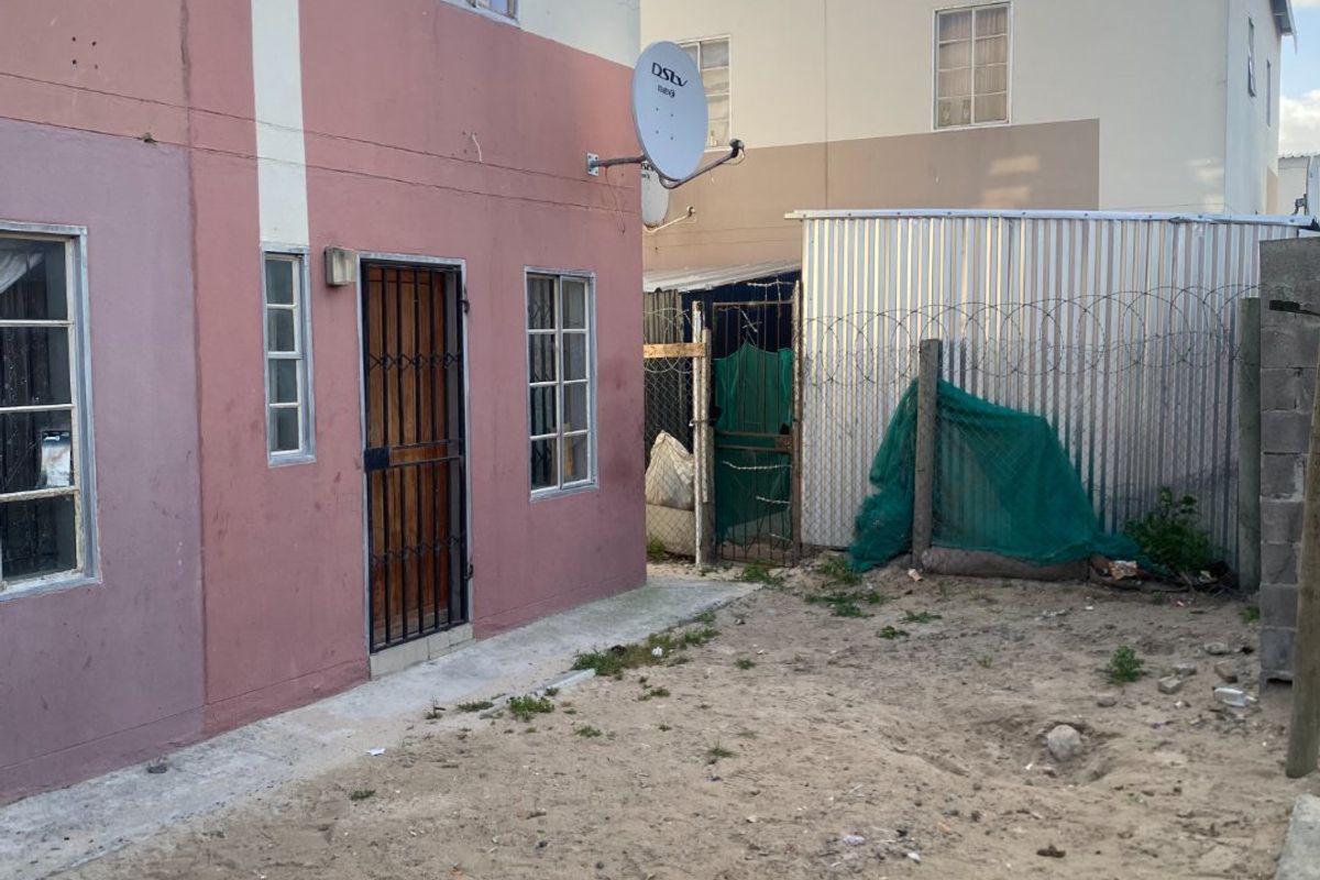 Rear exterior view of a two-story residential property featuring a sandy yard, security gate, and perimeter fencing with razor wire.