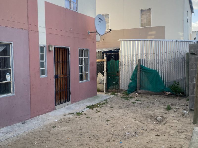 Rear exterior view of a two-story residential property featuring a sandy yard, security gate, and perimeter fencing with razor wire.