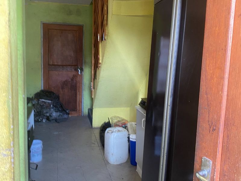 A utility space or storage area featuring tiled flooring and access to an internal staircase, currently in need of cosmetic refurbishment.