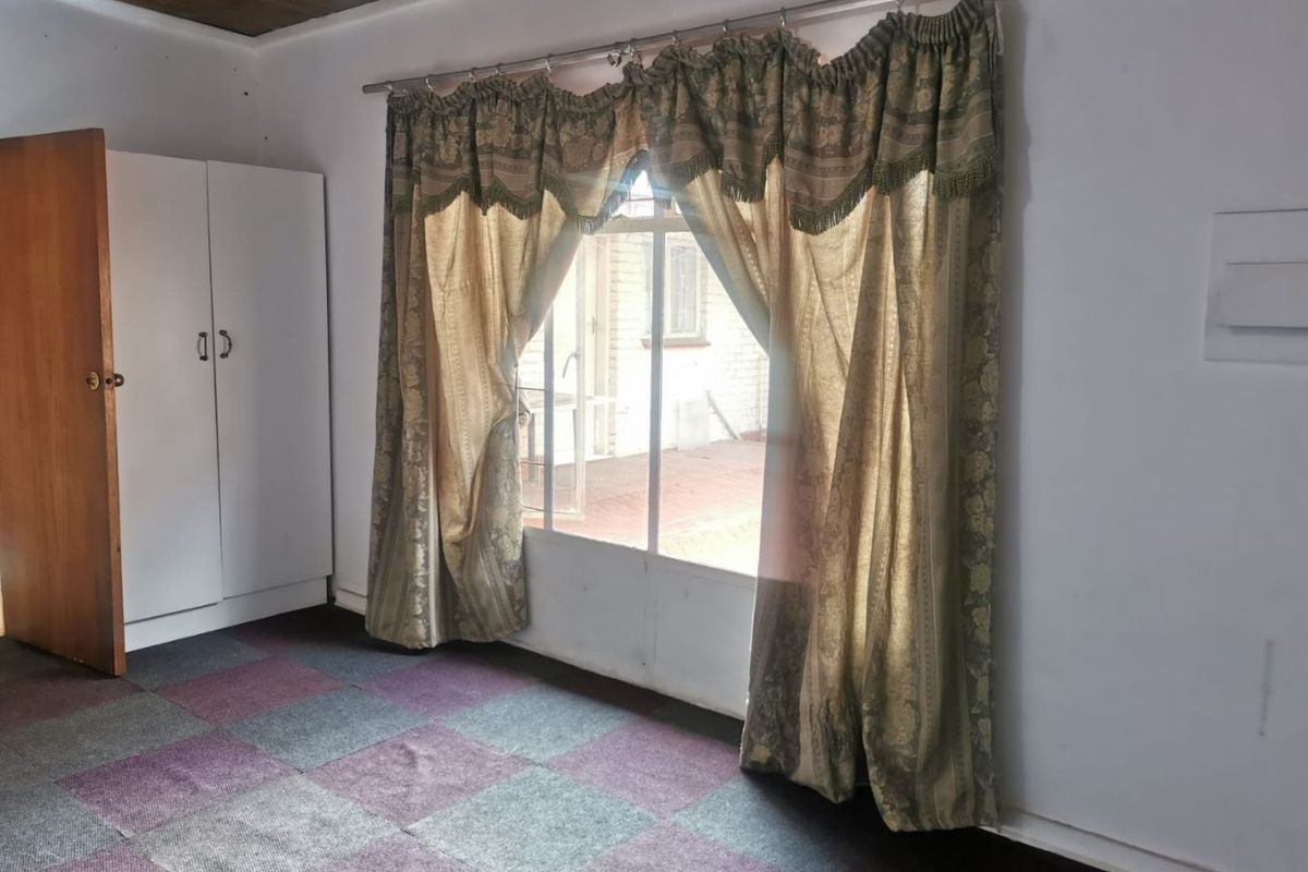 A bedroom featuring a built-in wardrobe, timber ceiling, and carpet tile flooring, with direct access to an outdoor area through a large window.