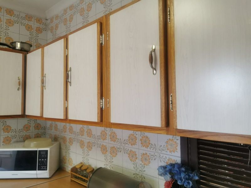 A kitchen area featuring dated patterned wall tiles and traditional laminate cabinetry with wood-look trim.