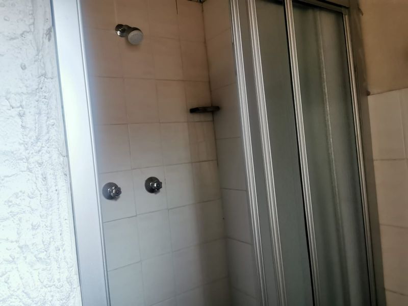 A dated shower enclosure featuring white wall tiles, a sliding glass door, and standard chrome shower fixtures.