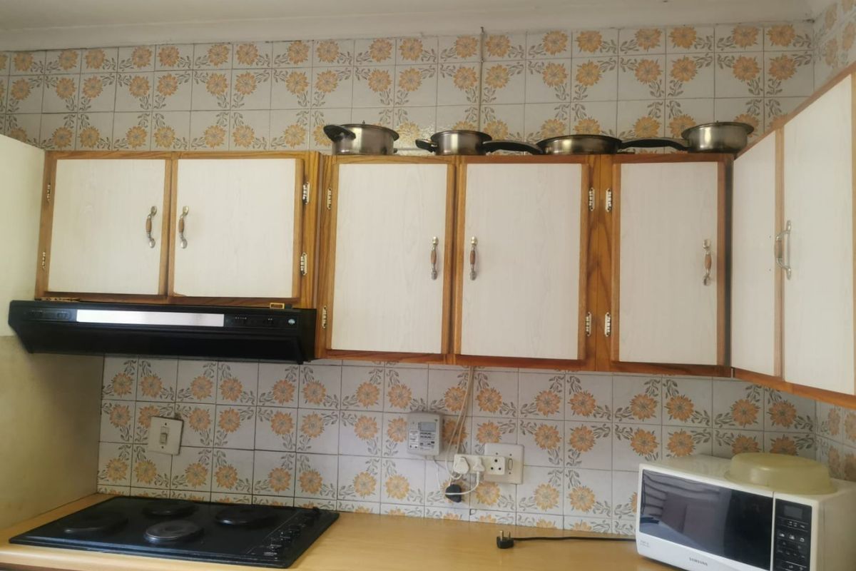 A functional kitchen featuring dated floral wall tiles, laminate countertops, and built-in cabinetry with an integrated electric hob and extractor fan.