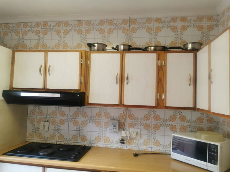 A functional kitchen featuring dated floral wall tiles, laminate countertops, and built-in cabinetry with an integrated electric hob and extractor fan.