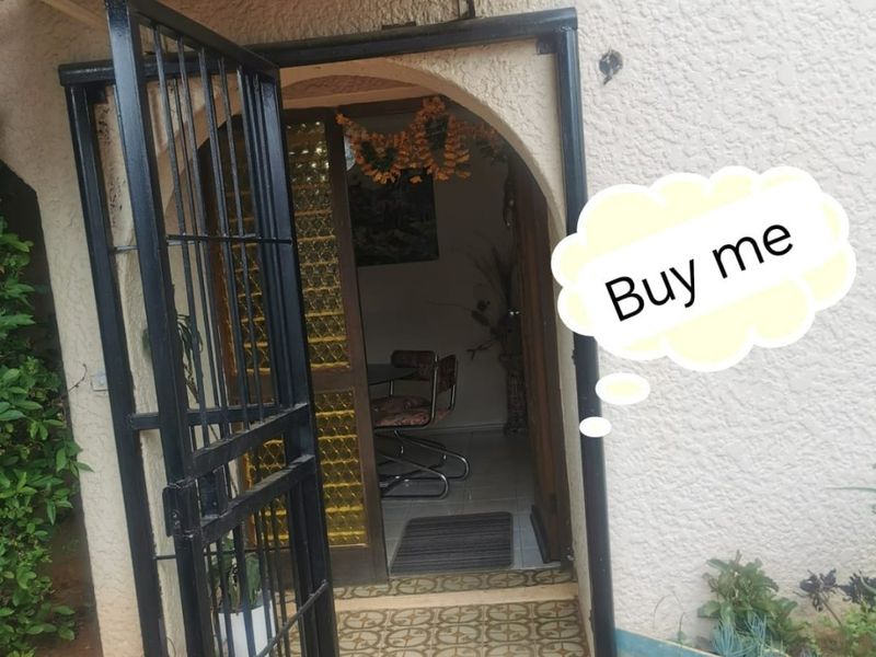 Entrance area featuring a security gate, arched doorway, and patterned floor tiles, showing signs of wear on the exterior wall.