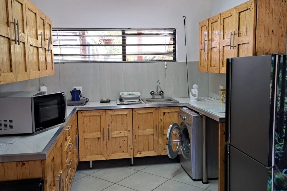 Functional kitchen featuring wooden cabinetry, tiled flooring, a stainless steel sink, and dedicated space for laundry appliances.