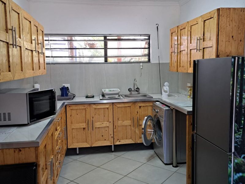 Functional kitchen featuring wooden cabinetry, tiled flooring, a stainless steel sink, and dedicated space for laundry appliances.