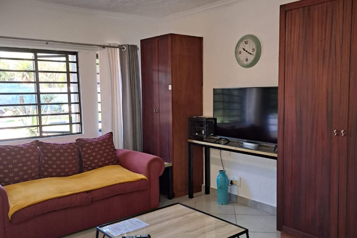 A living room featuring tiled flooring, built-in wooden cabinetry, and security bars on the window, offering a functional space with potential for modernization.