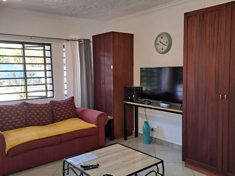A living room featuring tiled flooring, built-in wooden cabinetry, and security bars on the window, offering a functional space with potential for modernization.