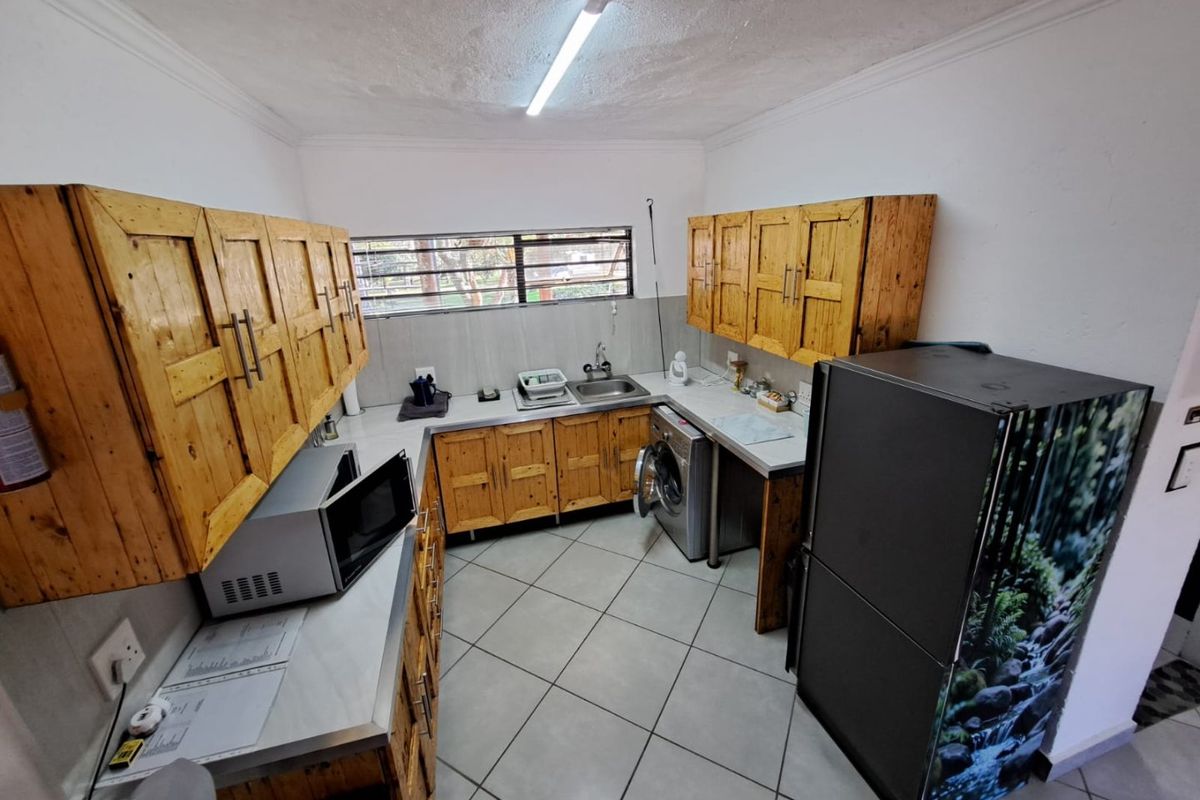 A functional kitchen featuring wooden cabinetry, tiled flooring, and a stainless steel sink, offering a practical layout for daily use.