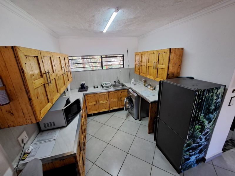 A functional kitchen featuring wooden cabinetry, tiled flooring, and a stainless steel sink, offering a practical layout for daily use.