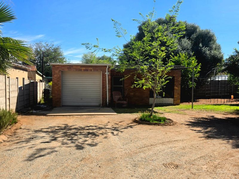 Front view of a brick house featuring a single roll-up garage door and an unpaved driveway area.
