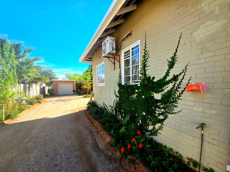 Side view of the property showing a brick facade, security-barred windows, an external air conditioning unit, and a gravel driveway leading to a detached garage.