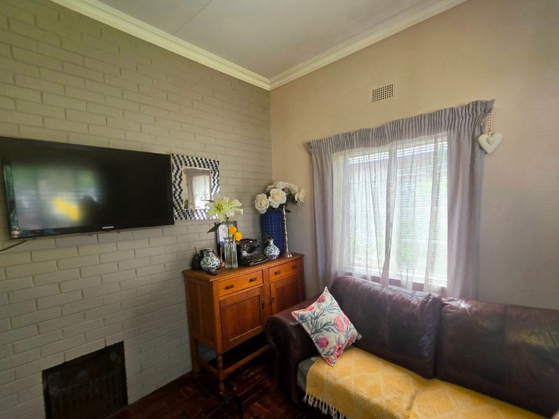 A cozy living room featuring a painted brick fireplace, crown molding, and classic parquet flooring, offering a warm and inviting atmosphere.