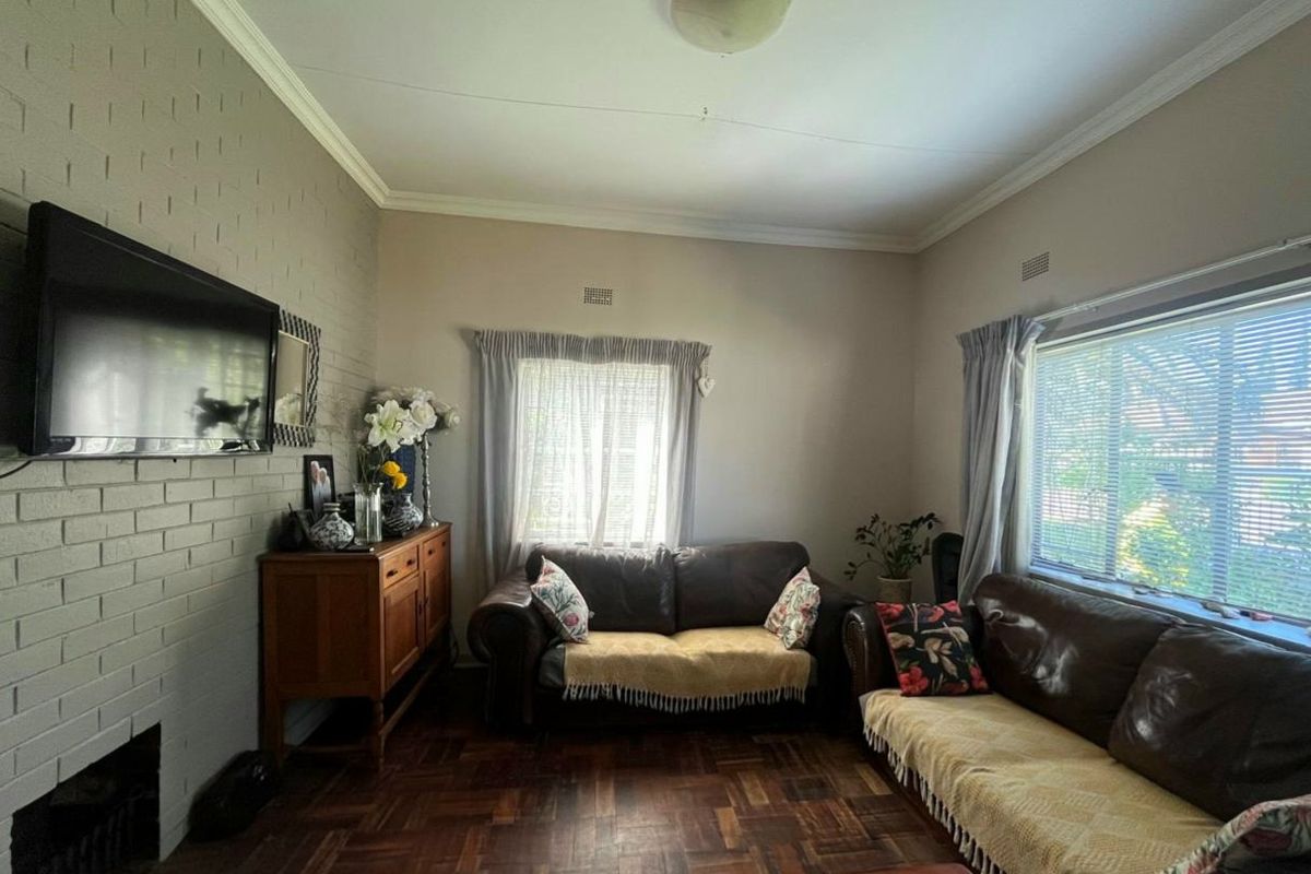 A cozy living room featuring classic parquet flooring, a painted brick fireplace, and large windows that provide natural light.