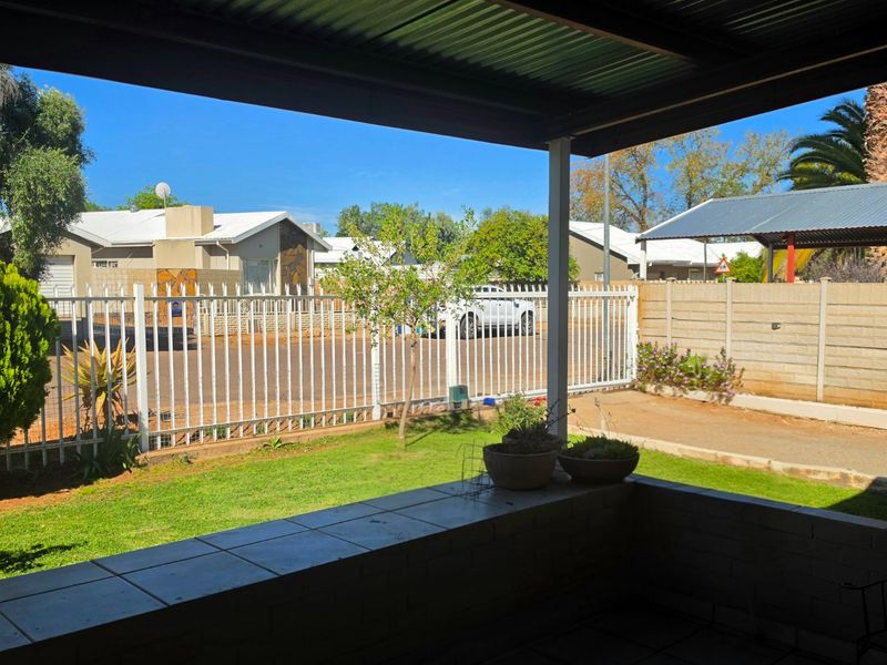 A covered patio area overlooking a private garden with a tiled surface and metal roofing, enclosed by a secure boundary fence.