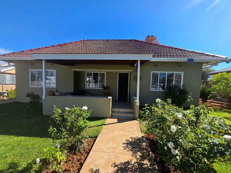 Front view of a single-story brick house featuring a tiled roof, a covered entrance porch, and a landscaped front garden with a concrete walkway.