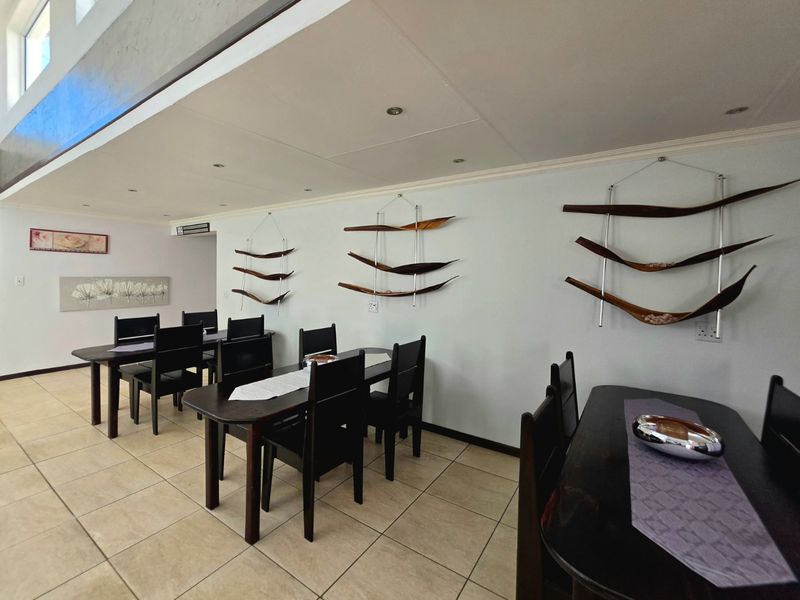 A spacious dining area featuring neutral tiled flooring and recessed ceiling lighting, providing a functional space for formal dining and entertaining.