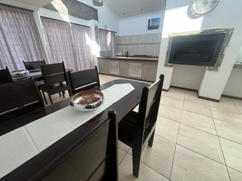 Open-plan living and dining area featuring tiled floors, a built-in fireplace, and a functional kitchen space with cabinetry.
