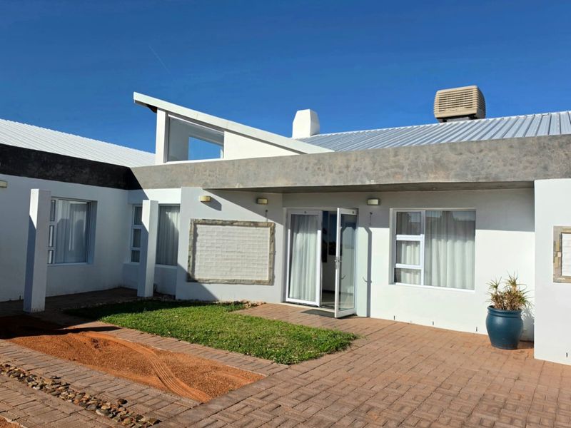 Rear exterior view of a modern home featuring a paved patio area, metal roofing, and large sliding glass doors leading into the residence.