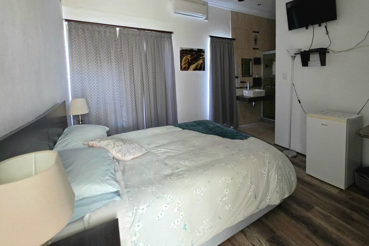 A bedroom featuring laminate flooring, a ceiling fan, a split-system air conditioner, and an open-plan en-suite bathroom area.