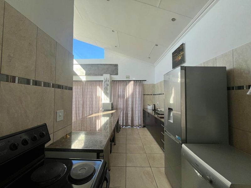 A functional kitchen featuring granite countertops, tiled splashbacks, and a vaulted ceiling with a skylight, providing ample natural light and workspace.
