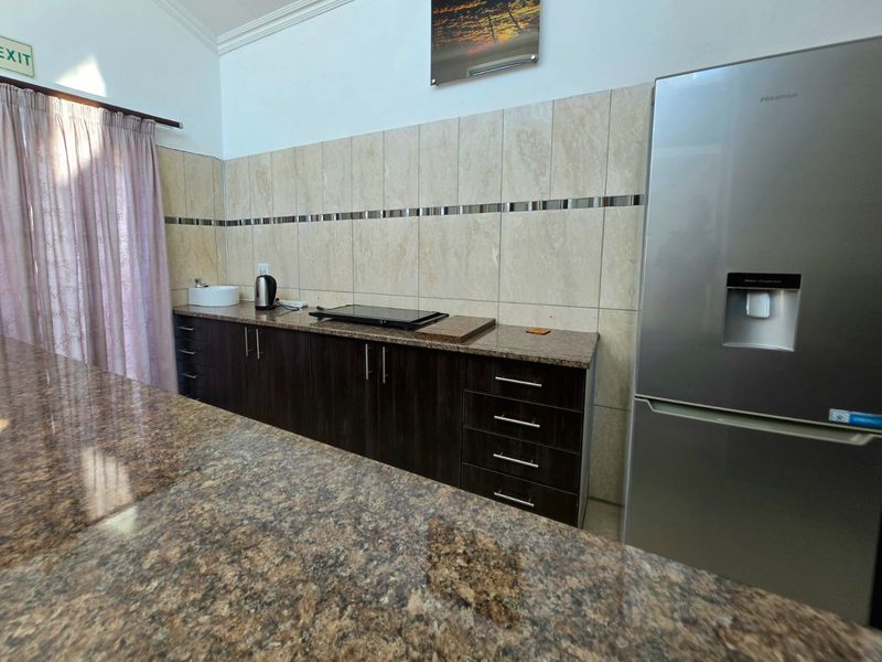 A functional kitchen featuring dark wood cabinetry, granite countertops, a tiled backsplash, and a built-in hob with an integrated stainless steel refrigerator.