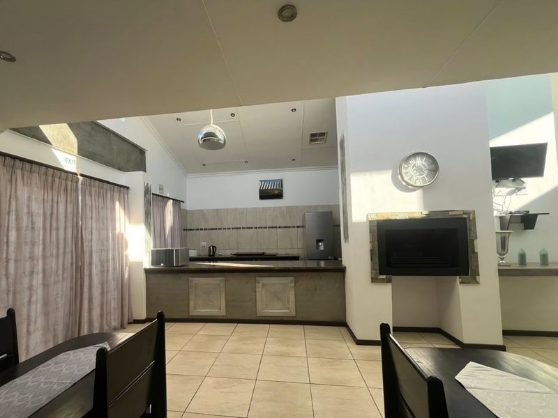 Spacious open-plan living area featuring a built-in fireplace, tiled flooring, and a functional kitchen with a breakfast bar and neutral finishes.