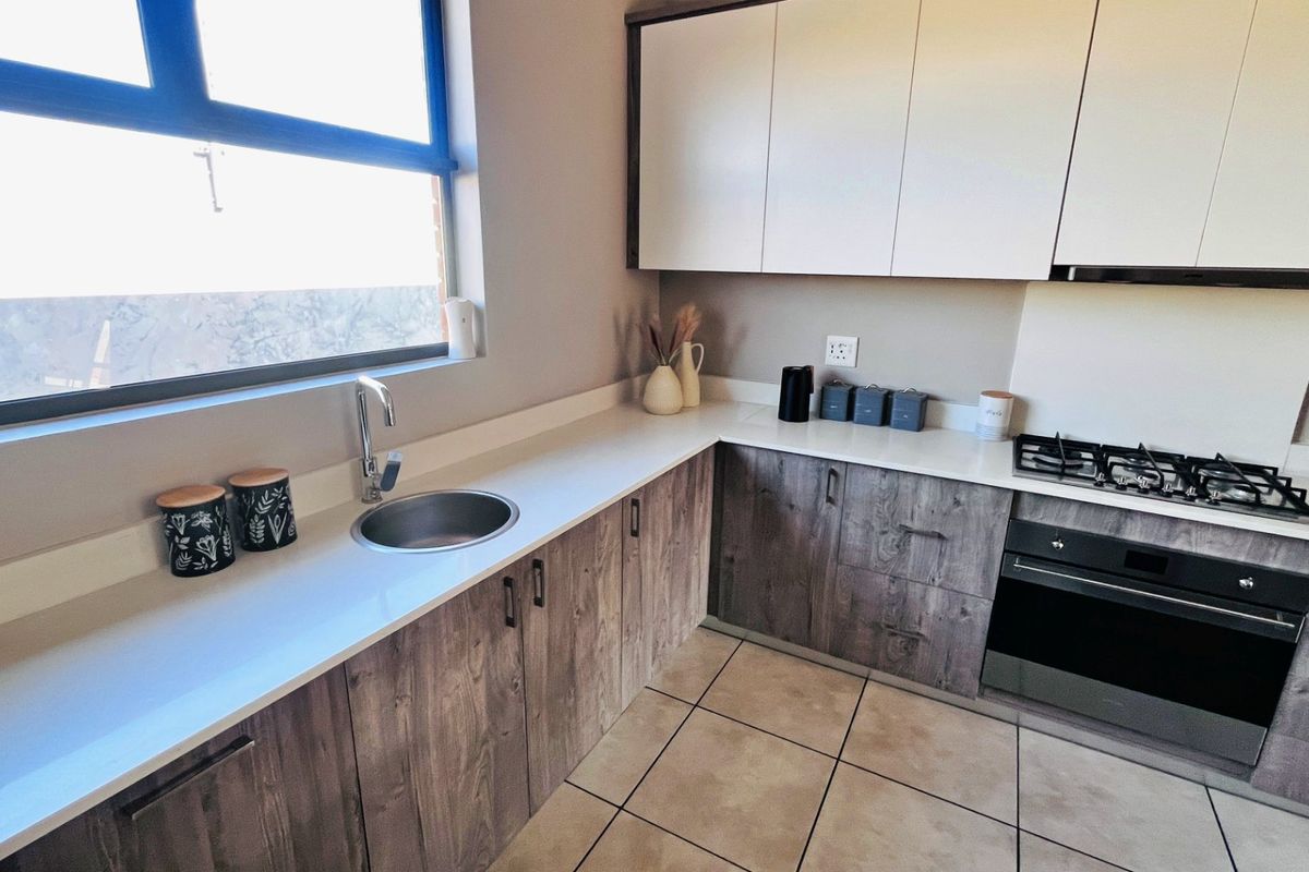 Modern kitchen featuring wood-grain lower cabinetry, white upper cabinets, stone countertops, gas hob, built-in oven, and tiled flooring.