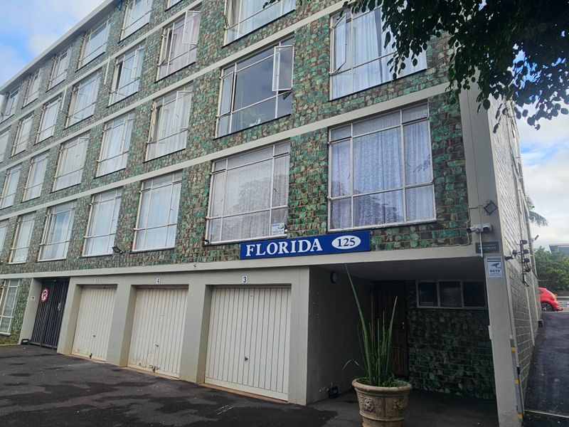 Exterior view of the Florida apartment building featuring a tiled facade, ground-level garage access, and paved driveway area.