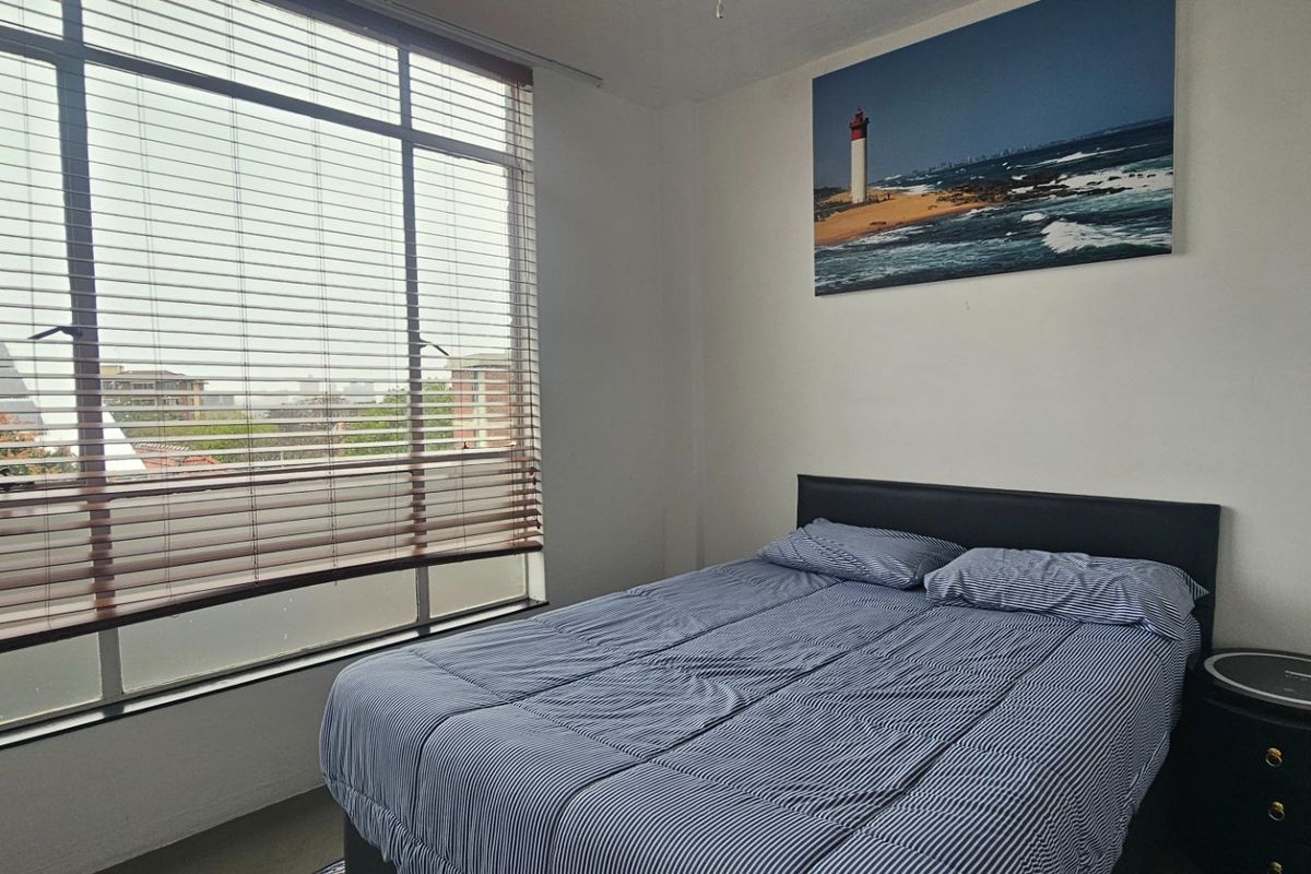A bedroom featuring a large window with venetian blinds, providing natural light and an exterior view.