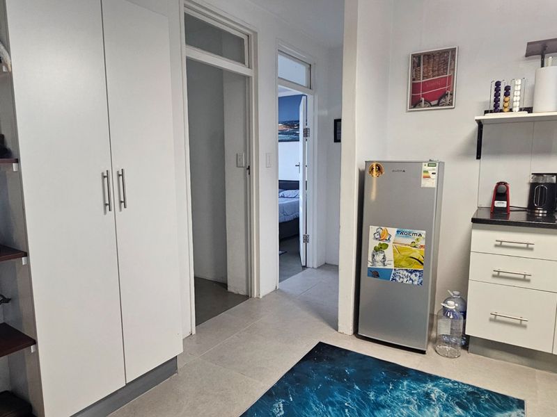 A compact kitchen area featuring white built-in cabinetry, dark countertops, and tiled flooring, with direct access to adjacent rooms.