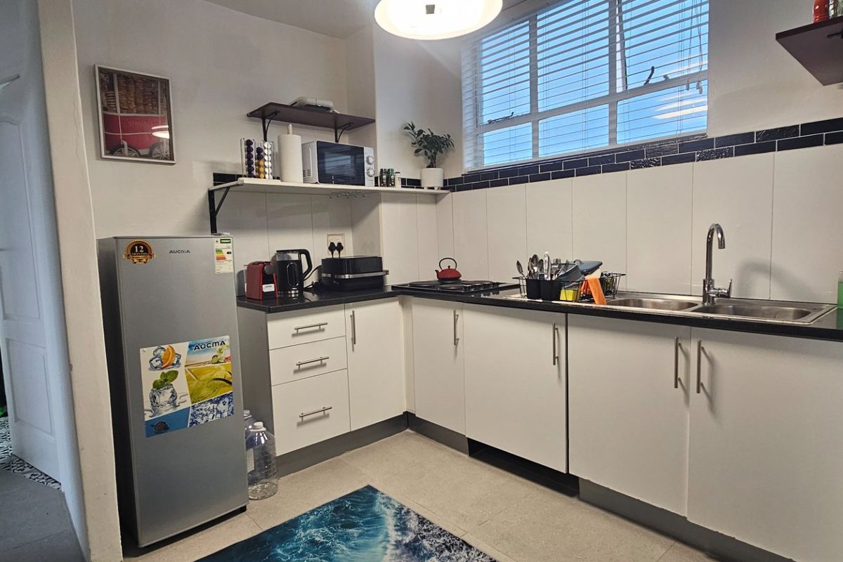 A functional kitchen featuring white cabinetry, dark countertops, a double sink, and a tiled backsplash with natural light from the window.
