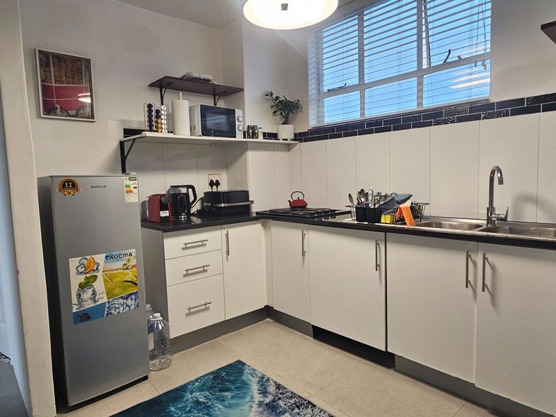 A functional kitchen featuring white cabinetry, dark countertops, a double sink, and a tiled backsplash with natural light from the window.